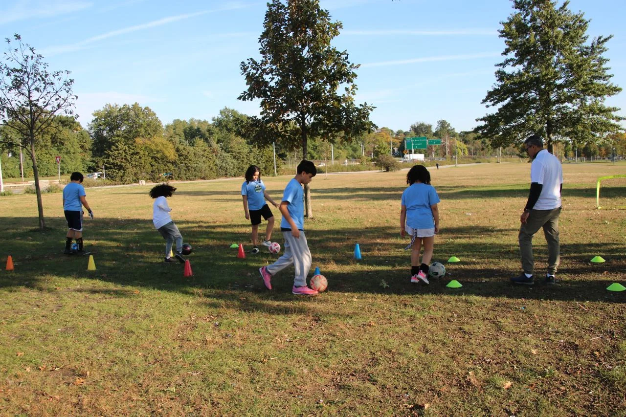 Children practicing soccer with a coach among colorful cones on an outdoor grass field