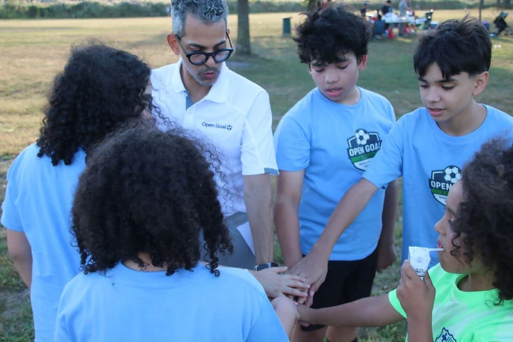 Open Goal players and a coach bringing their hands together in a team huddle